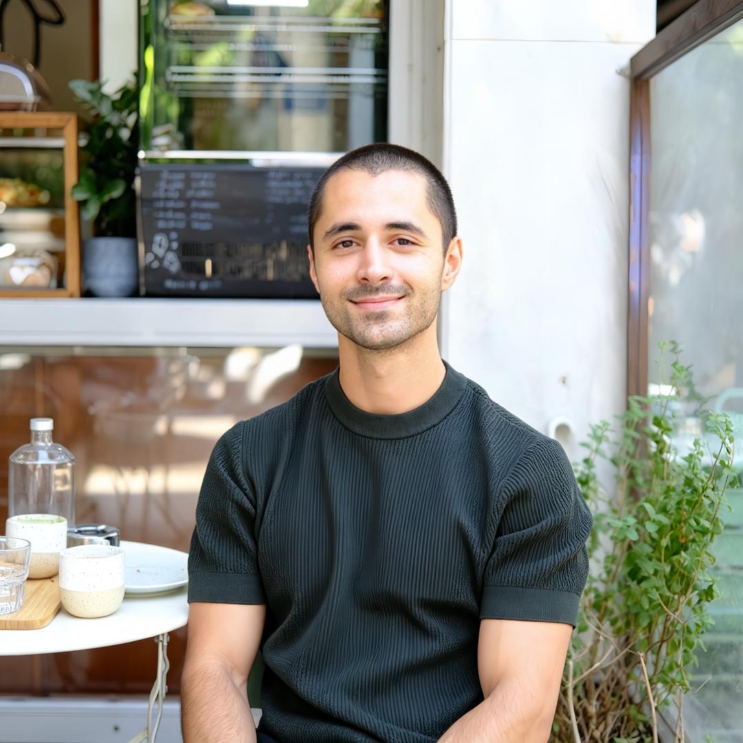 Alonso R., seated at a caf&eacute; table, smiling at the camera